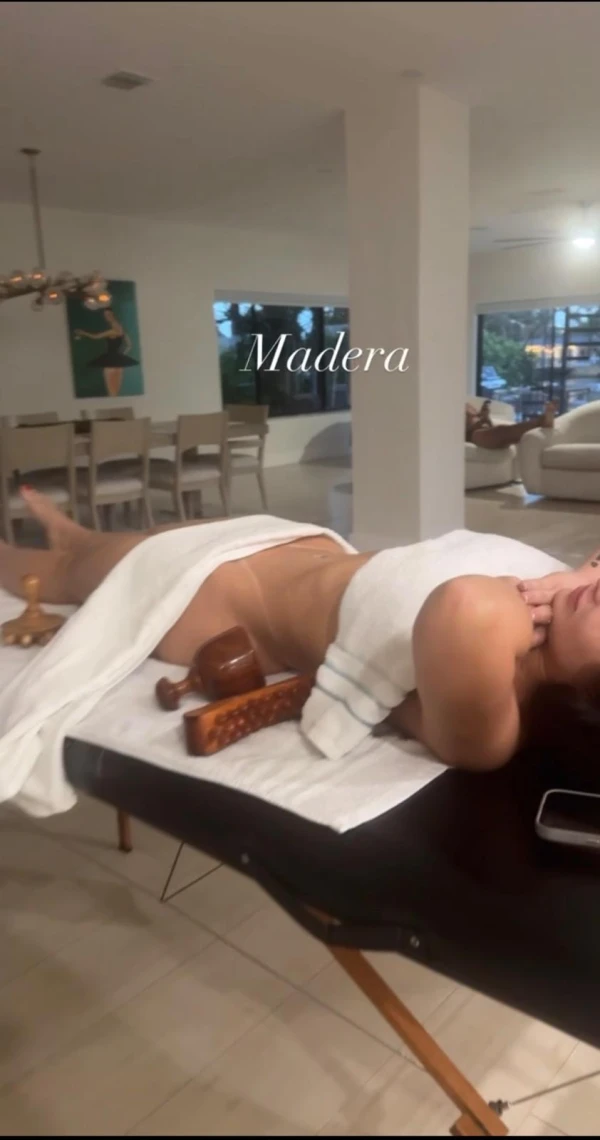Client resting on a treatment table with wooden sculpting tools beside the waist